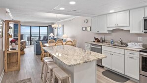Cozinha moderna com armários brancos, bancada de granito e área de jantar com uma ilha grande e banquetas.