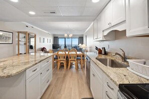 Enjoy meals in the kitchen with a granite countertop and stainless steel appliances, adjacent to a dining area with a wooden table and chandelier.