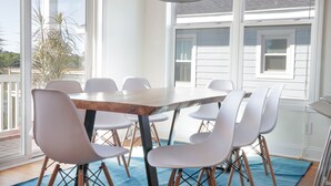 A dining area with a wooden table and white chairs, large windows, and a blue rug. - Short walk to the Beach 5 BR Beach House with a Private Pool! Marsh Mellow (Murrells Inlet)
