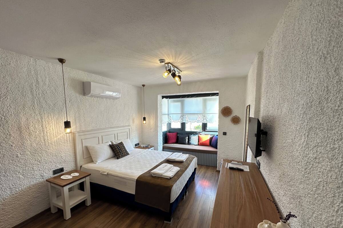 A bedroom with a bed, bedside tables, a desk, a TV, and a window with a view.