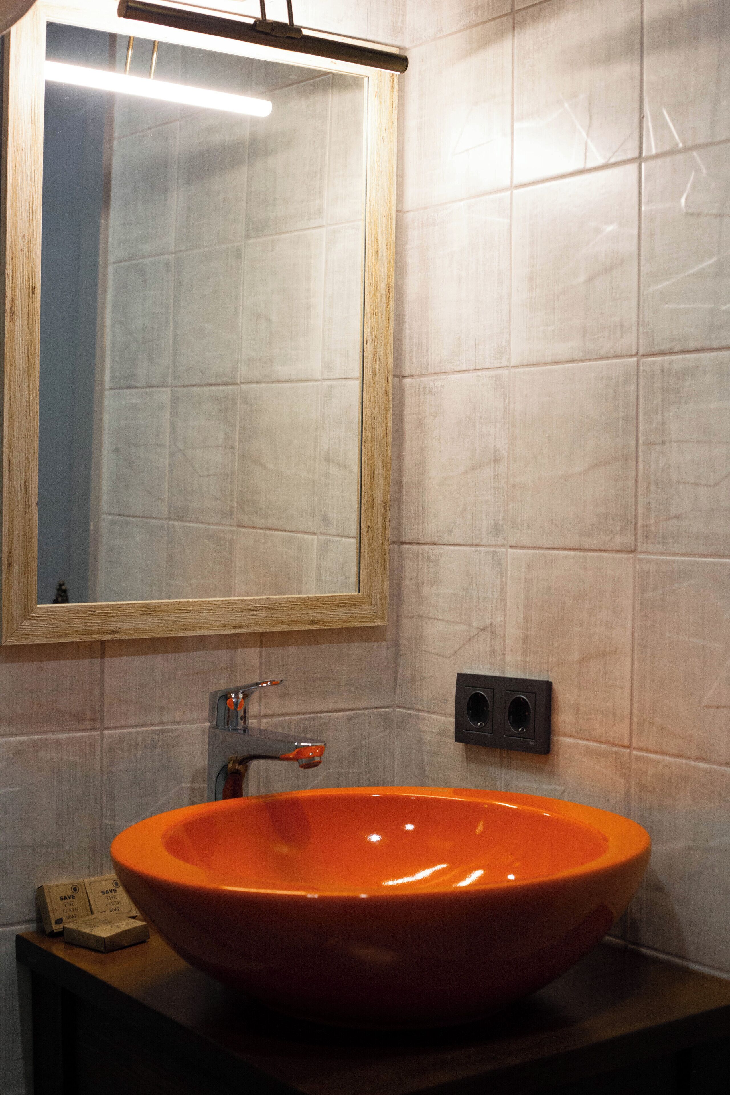 A bathroom with a large orange sink, a mirror, and a light fixture above the mirror.