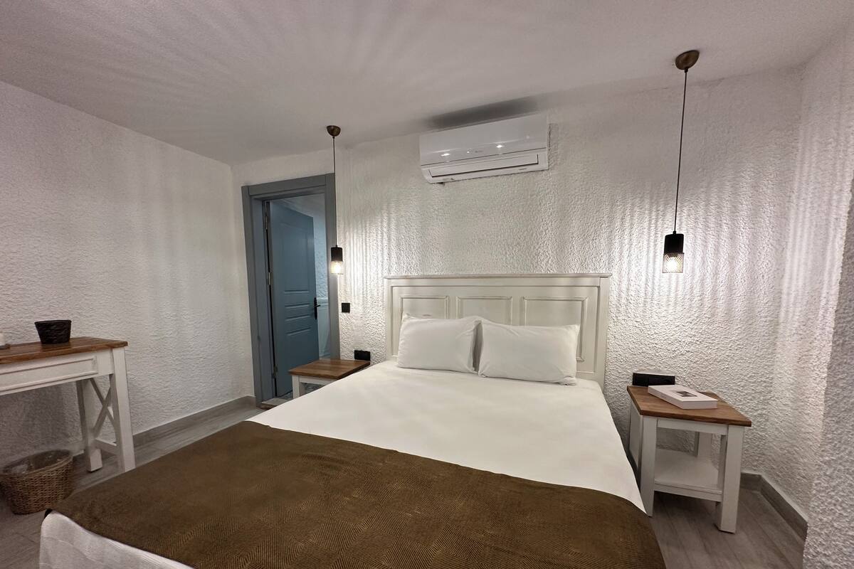 A neatly arranged bedroom with a large bed, bedside tables, a desk, and an air conditioning unit.