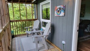 A covered porch with two Adirondack chairs, a window, and a colorful painting on the wall. - It`s all new at Village Sunset, sweet little hidea (Blowing Rock)