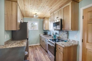 A compact kitchen with wooden cabinets, a granite countertop, a stainless steel stove, and a microwave. - It`s all new at Village Sunset, sweet little hidea (Blowing Rock)
