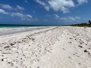 A sandy beach with footprints leading to the water, a clear sky, and a distant horizon. - Private Villa Directly on Windermere Beach, Private Pool, Tennis (Savannah Sound)