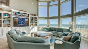 Een ruime woonkamer met een groot raam dat uitkijkt op het strand, een inbouwboekenplank en een comfortabele zithoek.