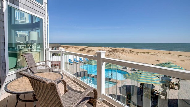 Een balkon met rieten meubilair, een glazen omheining en uitzicht op het strand en de zee.