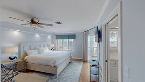 Une chambre à coucher comprenant un lit, des tables de chevet, un ventilateur de plafond, une fenêtre avec vue et un téléviseur fixé au mur.