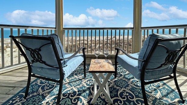 Un espace extérieur abrité, avec deux chaises et une petite table, donnant sur une plage.