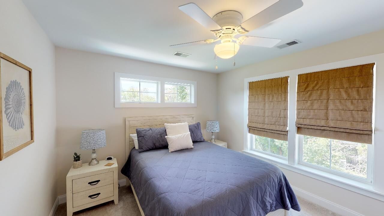 A bedroom with a bed, nightstands, a ceiling fan, and windows with blinds.