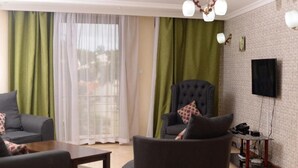 A living room with a sofa, armchair, and coffee table. There is a TV mounted on the wall and a small table with a telephone. - Stay.Plus Mount Kenya Road Nyali (Mombasa)
