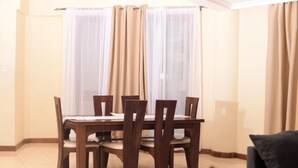 A dining area with a wooden table and chairs, beige curtains, and a tiled floor. - Stay.Plus Mount Kenya Road Nyali (Mombasa)