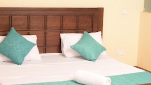 A neatly made bed with a wooden headboard, white bedding, and two teal pillows. - Stay.Plus Mount Kenya Road Nyali (Mombasa)