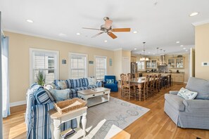 A spacious living room with a sofa, a dining area with a table and chairs, and a kitchen in the background.