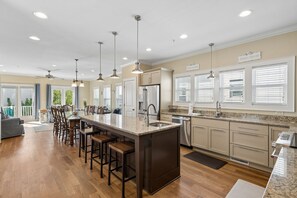 A spacious kitchen with a central island, bar stools, pendant lighting, and a view of the outdoors.
