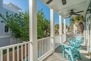 A covered porch with white railings, a ceiling fan, and blue Adirondack chairs.