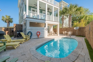 A two-story house with a swimming pool, outdoor furniture, and a wooden fence.