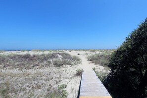 Un sentier sablonneux menant à une plage, avec une promenade en bois et une végétation clairsemée.