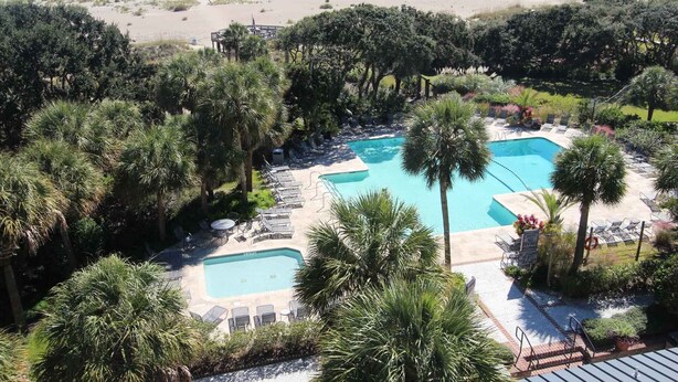A resort with two swimming pools surrounded by palm trees and lounge chairs, overlooking a beach. - Shipwatch A105: Oceanfront, private balcony & spectacular views in Wild Dunes (Isle of Palms)