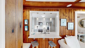 A modern kitchen with wooden paneling, a central island with stools, stainless steel appliances, and framed artwork on the walls.