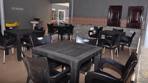 Restaurante com mesas e cadeiras de vime preto, um aviso de 'NÃO FUMAR' na parede e um muro de destaque em tijolo.