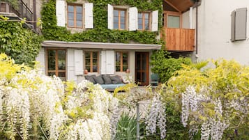 A two-story house with a balcony, a garden with white flowers, and a wooden fence.