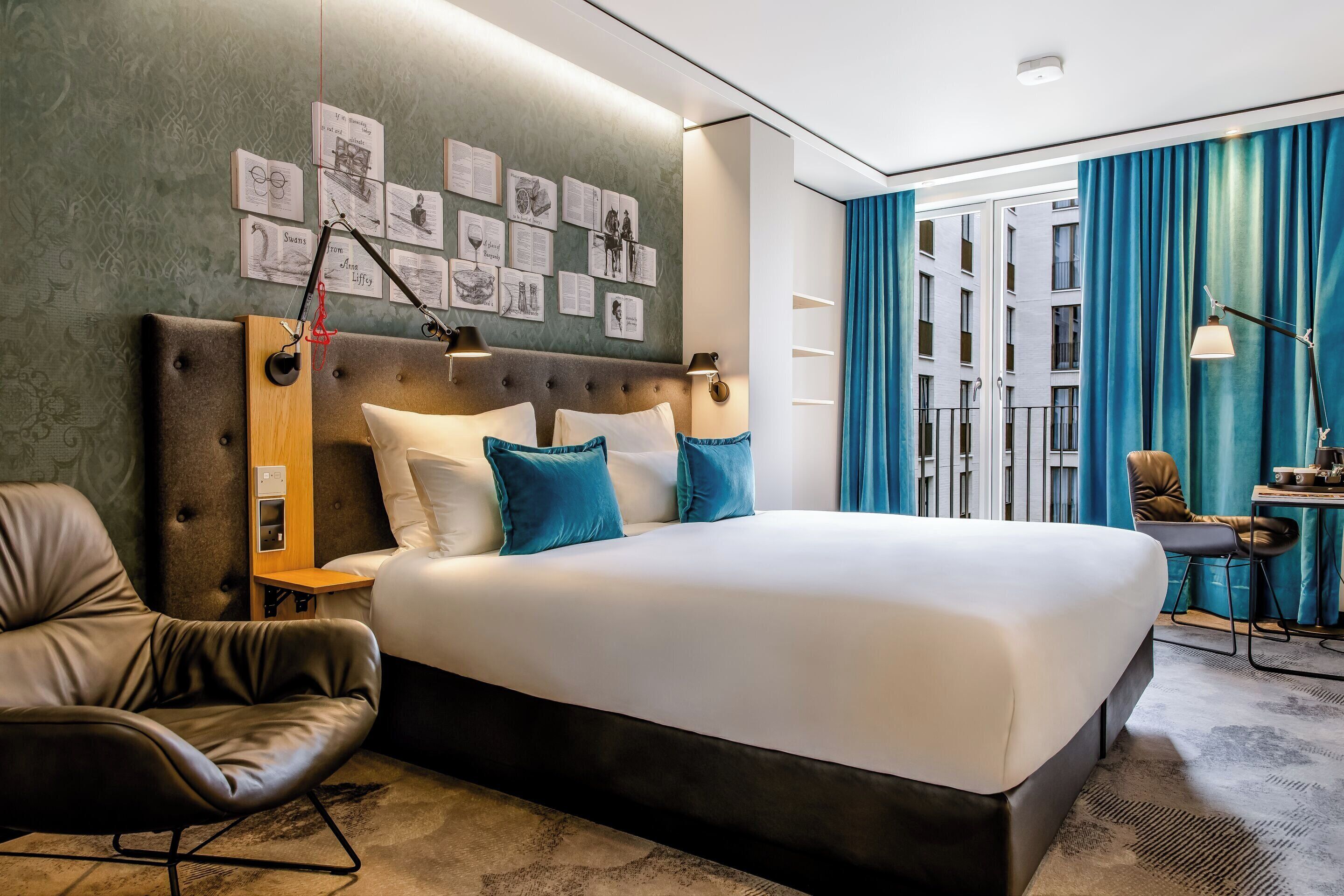 Ein modernes Hotelzimmer mit einem großen Bett, einem Ledersessel, einem Nachttisch und einer Wand mit gerahmten Bildern.