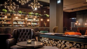 A bar area with leather chairs, a round table, and a wooden log display. - Motel One Dublin (Dublin)
