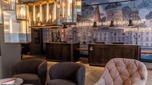 A modern interior with dark-toned armchairs, a tufted chair, and a cityscape mural. - Motel One Dublin (Dublin)