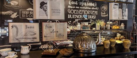 A coffee shop counter with a vintage aesthetic, featuring a teapot, cups, and a menu board with illustrations and text.