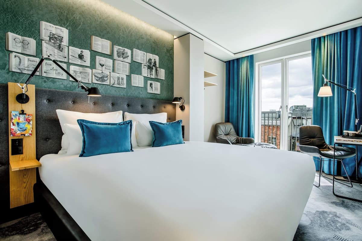 A modern hotel room with a large bed, a desk with a chair, and a city view through the window.