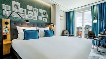 Habitación de hotel moderna con una cama grande, un escritorio con silla y vista a la ciudad a través del ventanal.