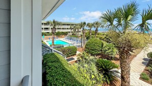 A pool area with lounge chairs and palm trees, overlooking a body of water. - Located in the heart of Isle of Palms with direct access to the oceanfront (Isle of Palms)
