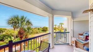 A balcony with a view of the beach, a wicker chair, and a staircase leading to the upper floor. - Located in the heart of Isle of Palms with direct access to the oceanfront (Isle of Palms)