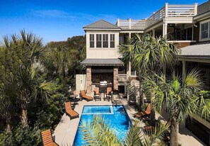 Une maison à deux étages avec une piscine dans le jardin, un espace salon extérieur et un coin barbecue.