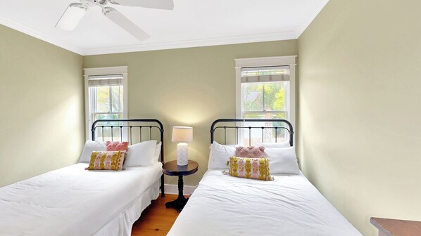 Une chambre double avec deux lits simples, une table de chevet avec une lampe et un ventilateur de plafond.