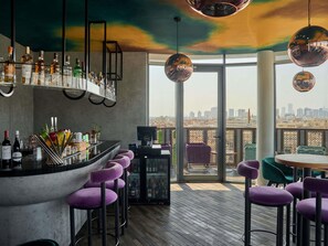 A bar area with a city view, bar stools, and a variety of bottles.