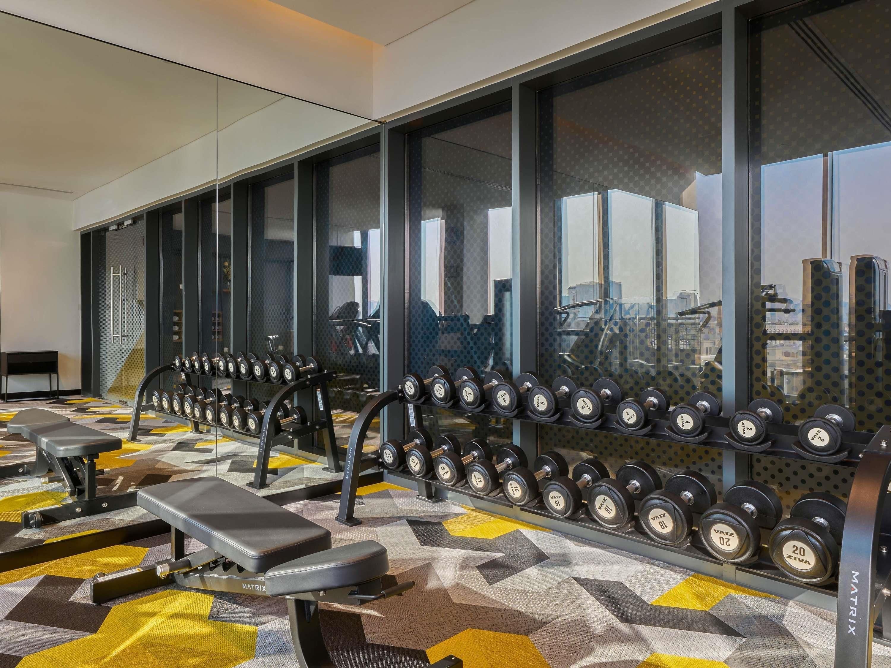 Un gimnasio con equipo de levantamiento de pesas, bancos y suelo estampado.