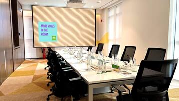 A conference room with a long table, black chairs, a projector screen, and a fire extinguisher.