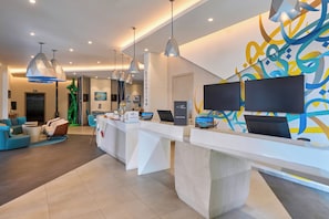 Uma área de recepção com balcão de check-in, espaço de espera e uma parede com arte abstrata.