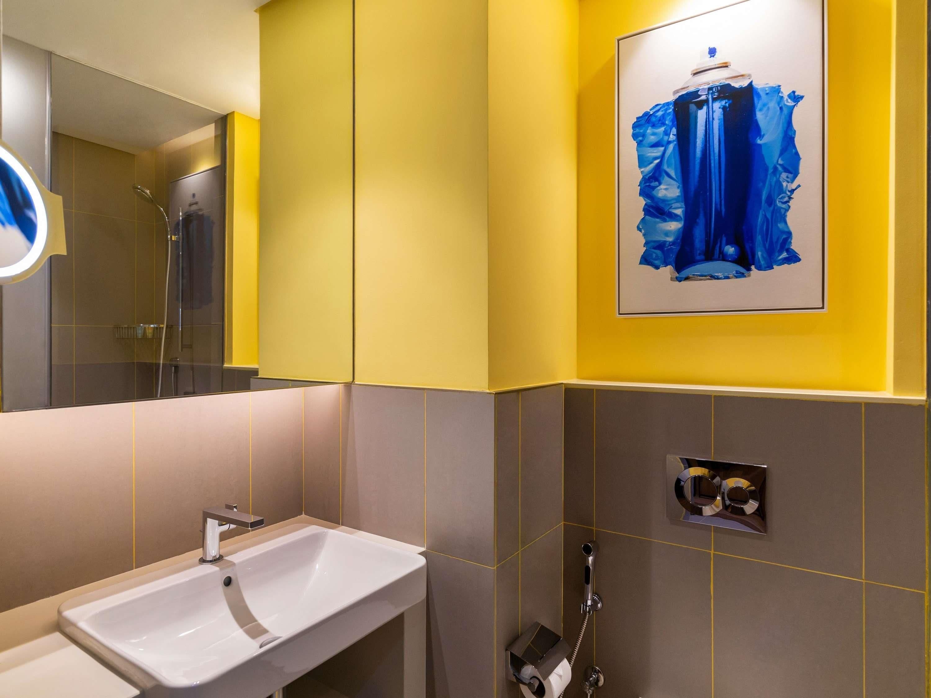 A bathroom with a white sink, a mirror, a shower, and a framed artwork on the wall.