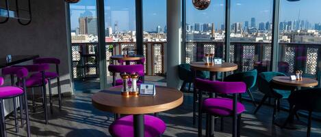 A modern indoor seating area with round tables and purple chairs, large windows offering a city view.