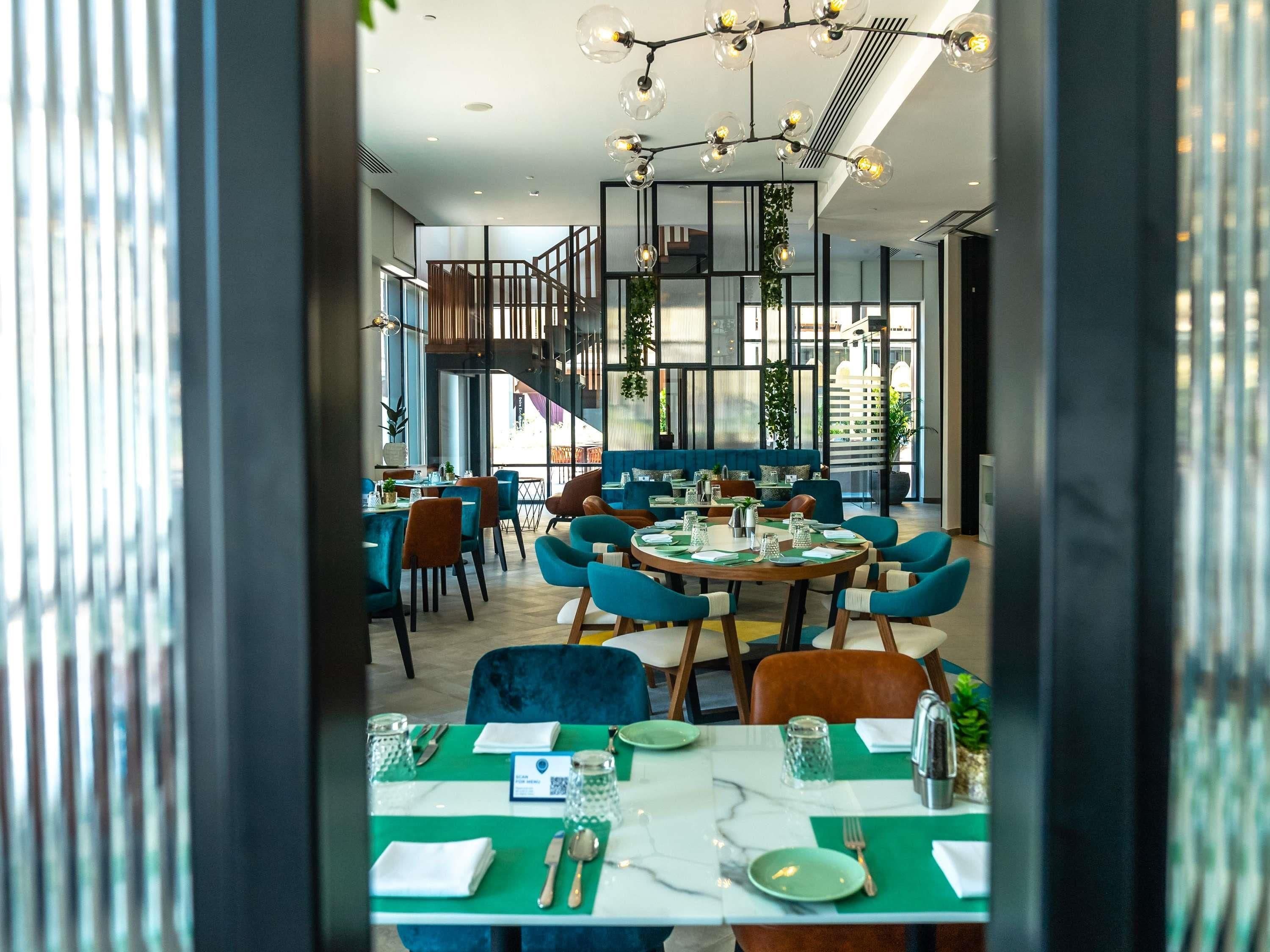 Un comedor moderno con mesas redondas, sillas azules y una escalera al fondo.