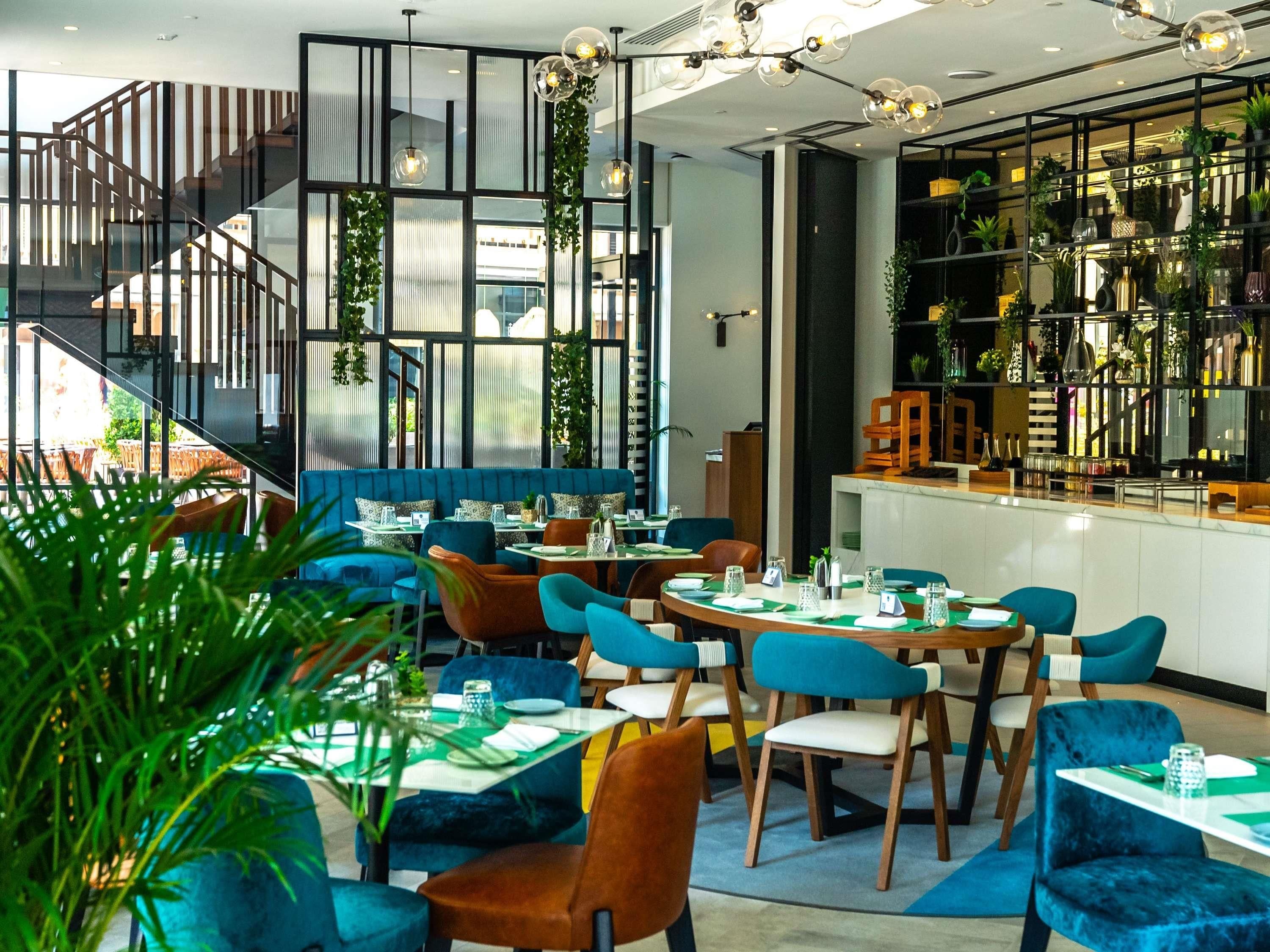 Ein modernes Restaurant mit verschiedenen Sitzgelegenheiten, darunter Tische und Boxen, sowie einer Treppe zu einer oberen Ebene.