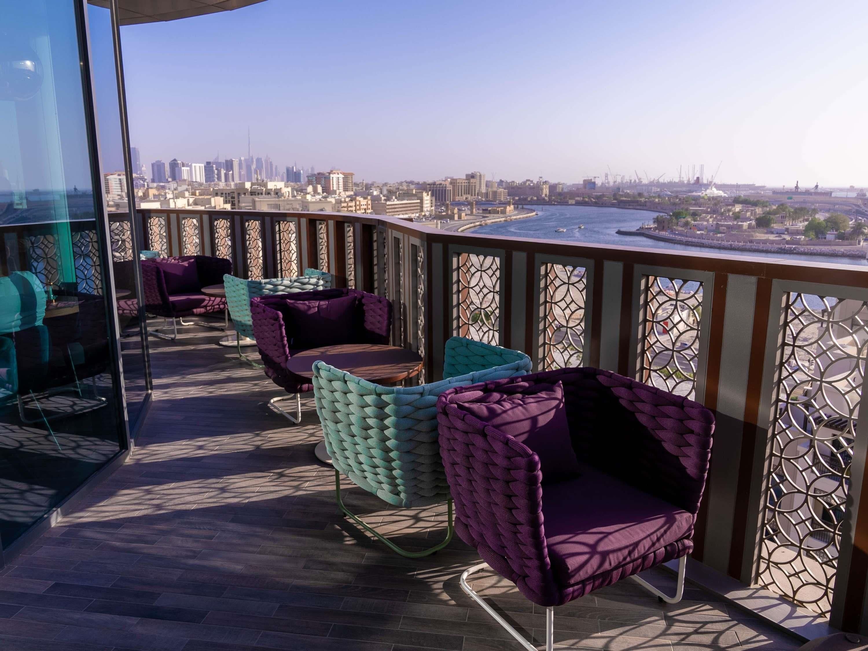 Un espace extérieur aménagé avec des chaises et des tables confortables, offrant une vue sur le paysage urbain, avec ses bâtiments et son front de mer.