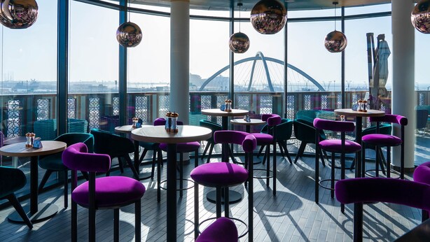 Moderni ravintola, jossa on pyöreät pöydät ja violetit tuolit, suuret ikkunat ja katosta roikkuvat diskopallot.