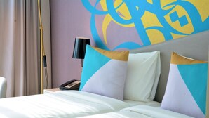 Hotelkamer met een bed, kussens, een nachtkastje, een lamp en een muur met abstracte kunst.
