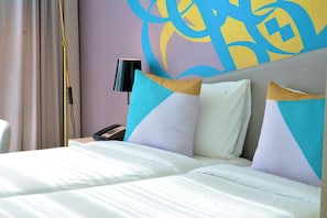 A hotel room with a bed, pillows, a nightstand, a lamp, and a wall with abstract art.