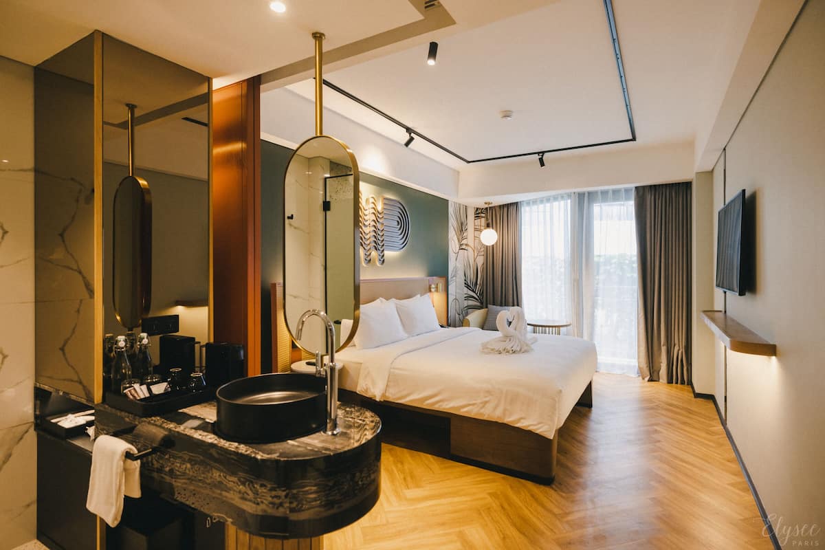 A modern hotel room with a large bed, a bathroom with a marble countertop, and a large mirror.