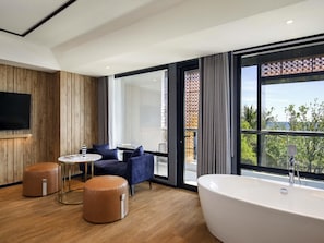 A modern room with a large window, a bathtub, a round table, and two ottomans. - Tribe Bali Kuta Beach (Kuta)